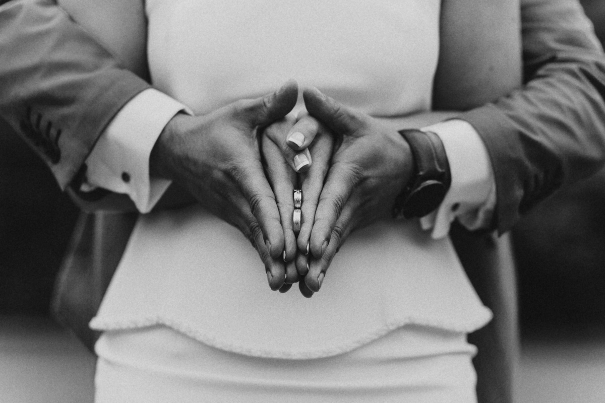 Schwarzweiße Hochzeitsfotografie von zwei Händen mit zwei Ringe in der Mitte in Herzform geformt.
